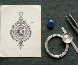 A pendant design sketch beside a blue stone, silver wire and a bezel cup