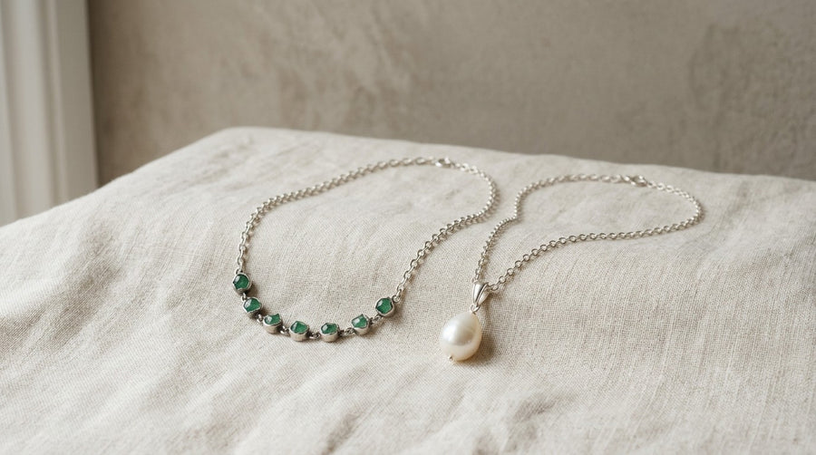 A silver emerald necklace and a pearl pendant on linen