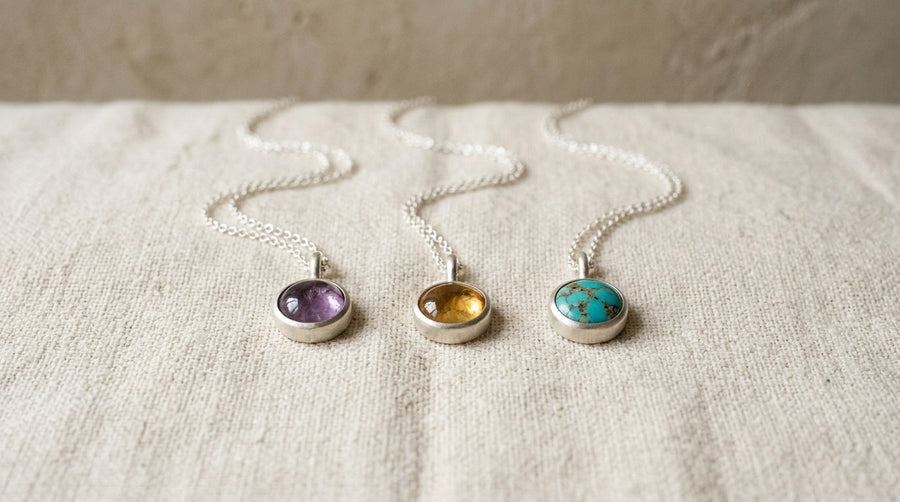 Three silver pendants with amethyst, citrine and turquoise on linen