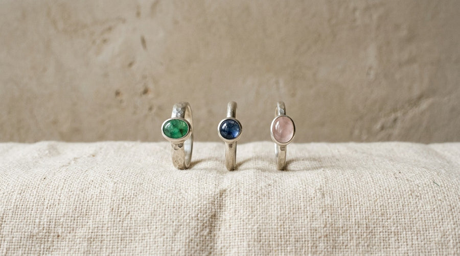 Three silver rings with emerald, sapphire and rose quartz on linen